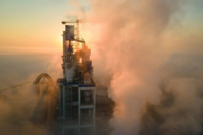 Industriële installatie in dichte rook bij zonsopgang, illustratief voor corrosieve en vervuilende rookgassen.