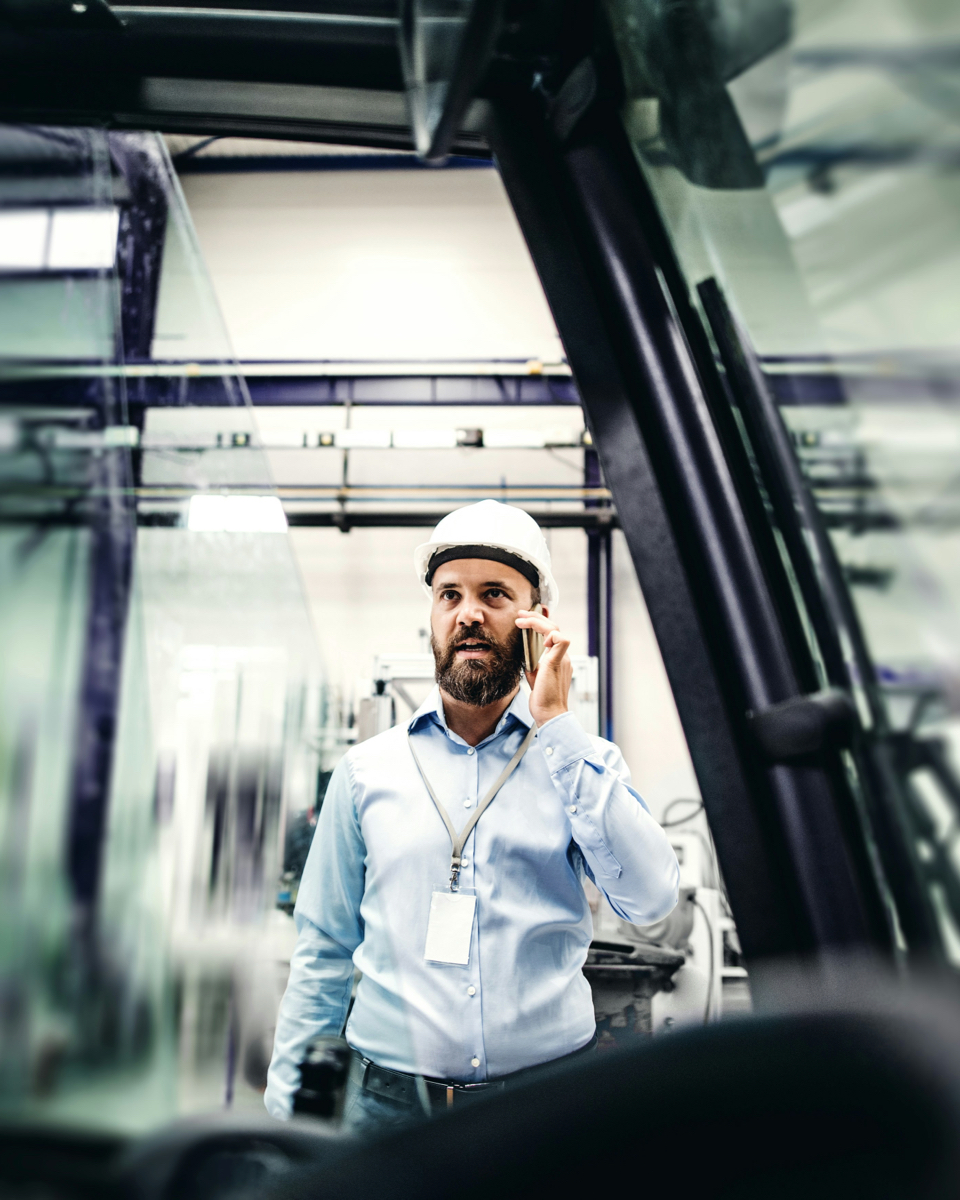 Technisch adviseur met helm voert telefoongesprek in fabriekshal over energiebesparing via warmteterugwinning