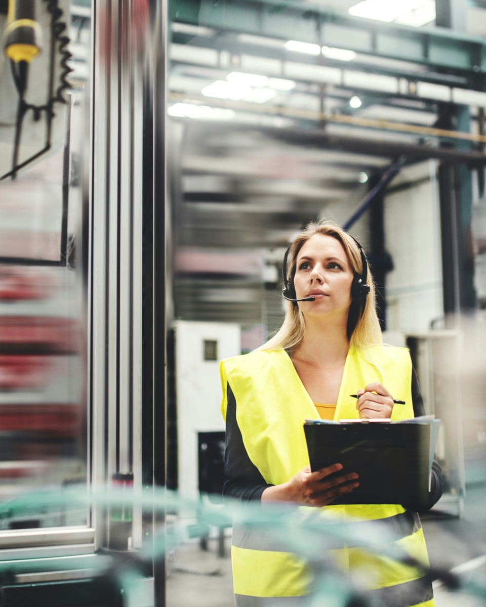 Vrouwelijke technicus in veiligheidsvest met headset voert inspectie uit in een industriële omgeving voor warmteterugwinning.