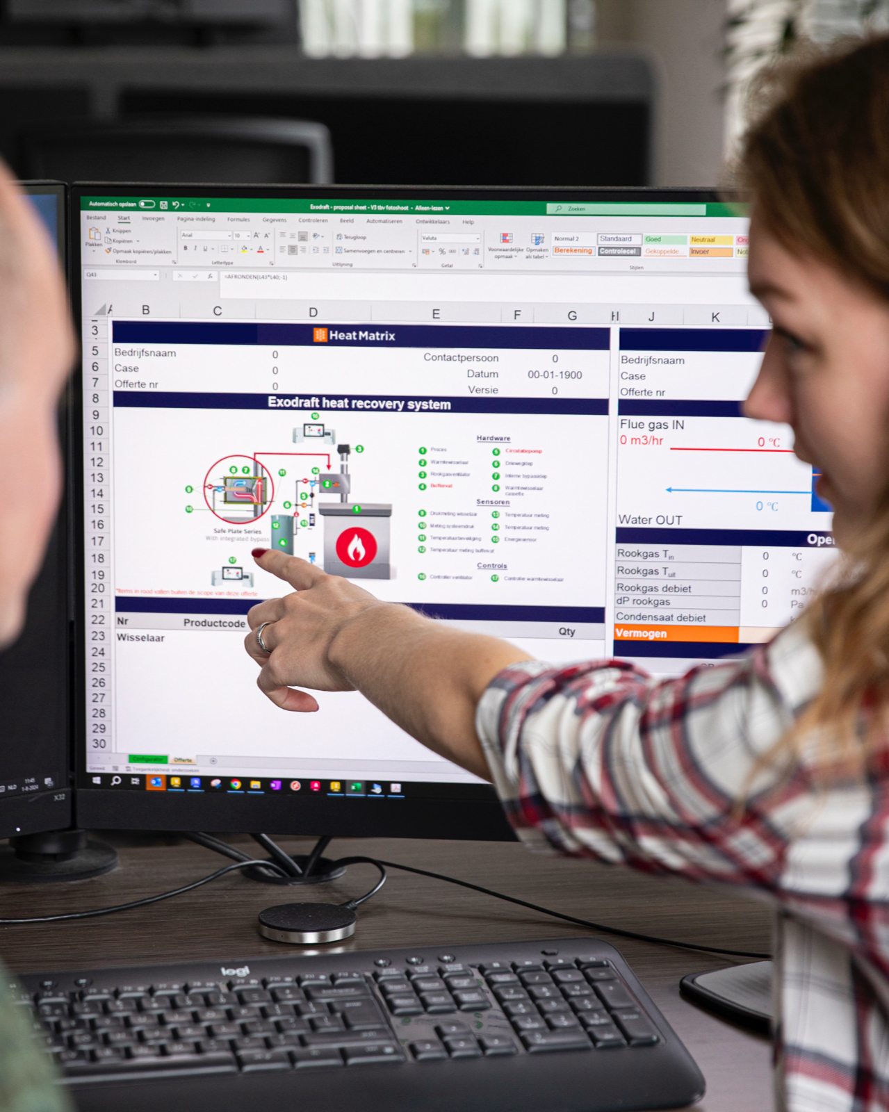 Twee medewerkers analyseren een technisch ontwerp voor een warmteterugwinningssysteem op computerscherm