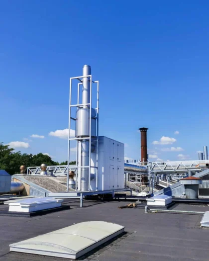 Warmteterugwinningsinstallatie van Exodraft op een industrieel dak met rookgasafvoer en leidingstructuur onder een heldere blauwe lucht.