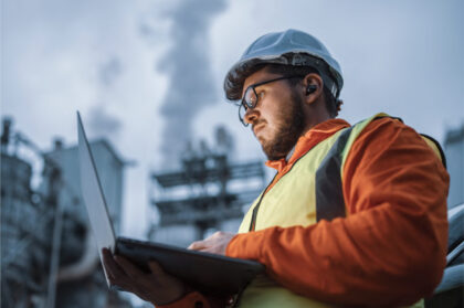 Technicus met veiligheidshelm en laptop voert inspectie uit op industriële locatie