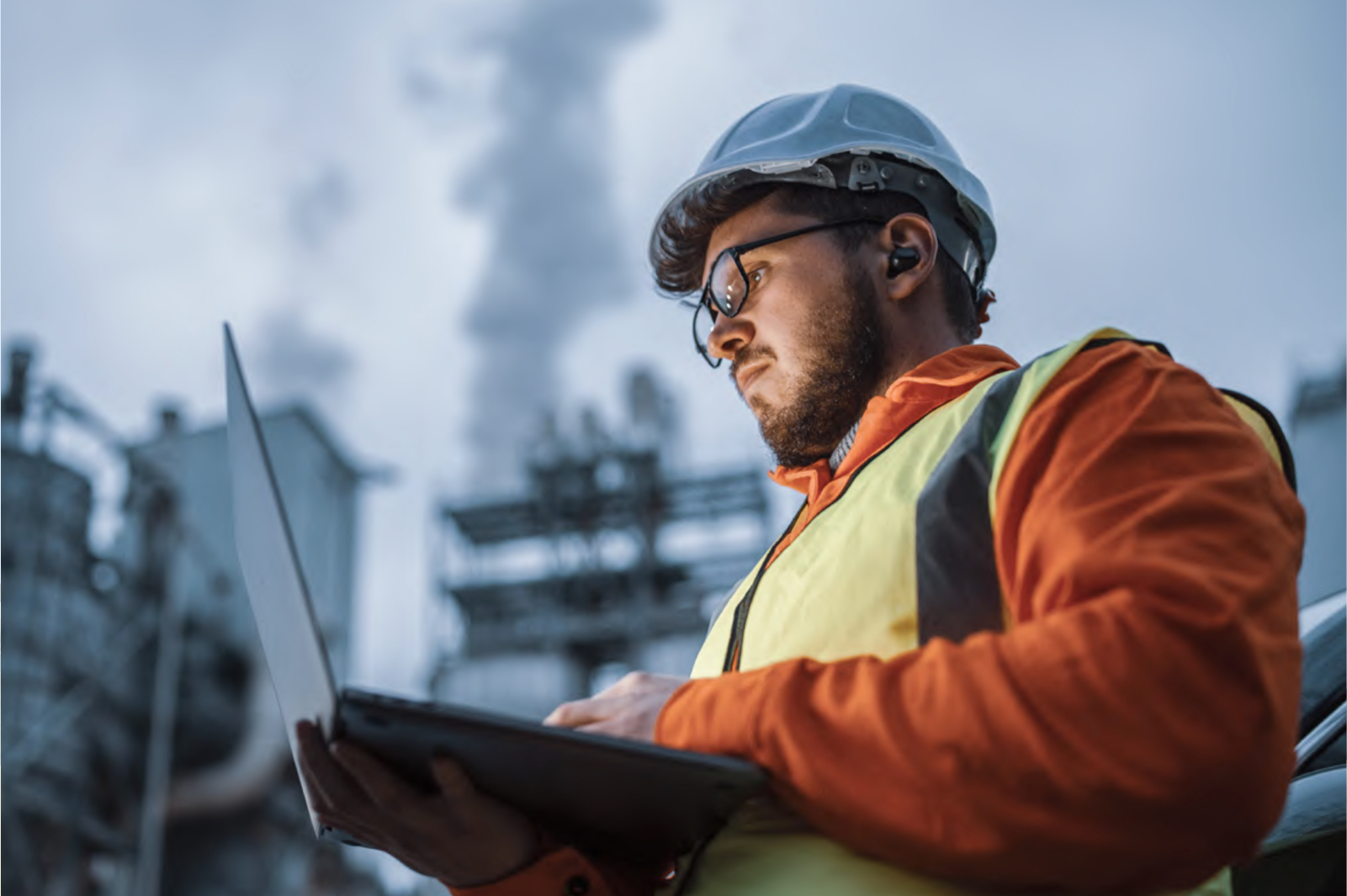 Technicus met veiligheidshelm en laptop voert inspectie uit op industriële locatie